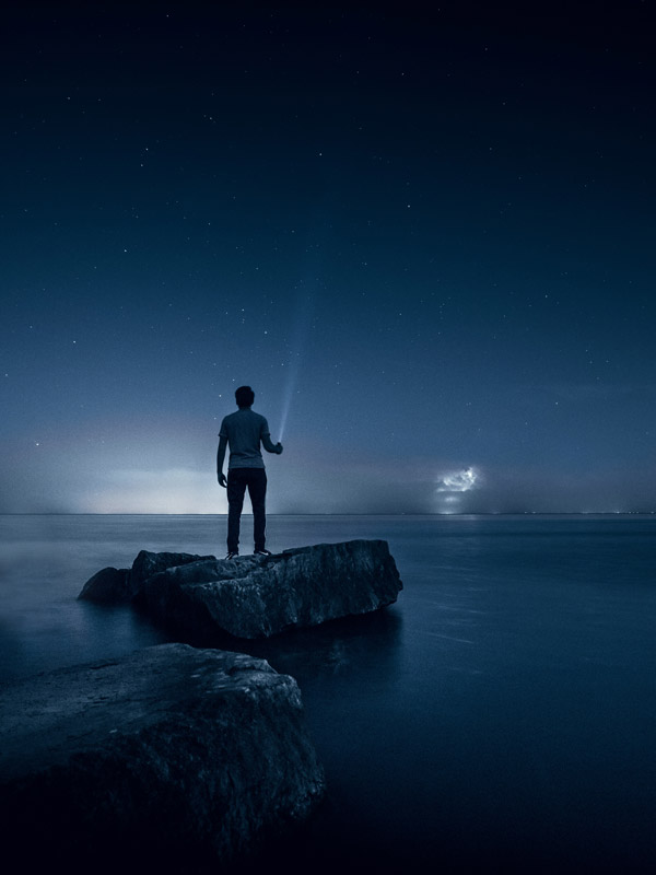 شخصی استاده روی سنگی در دریا در شب