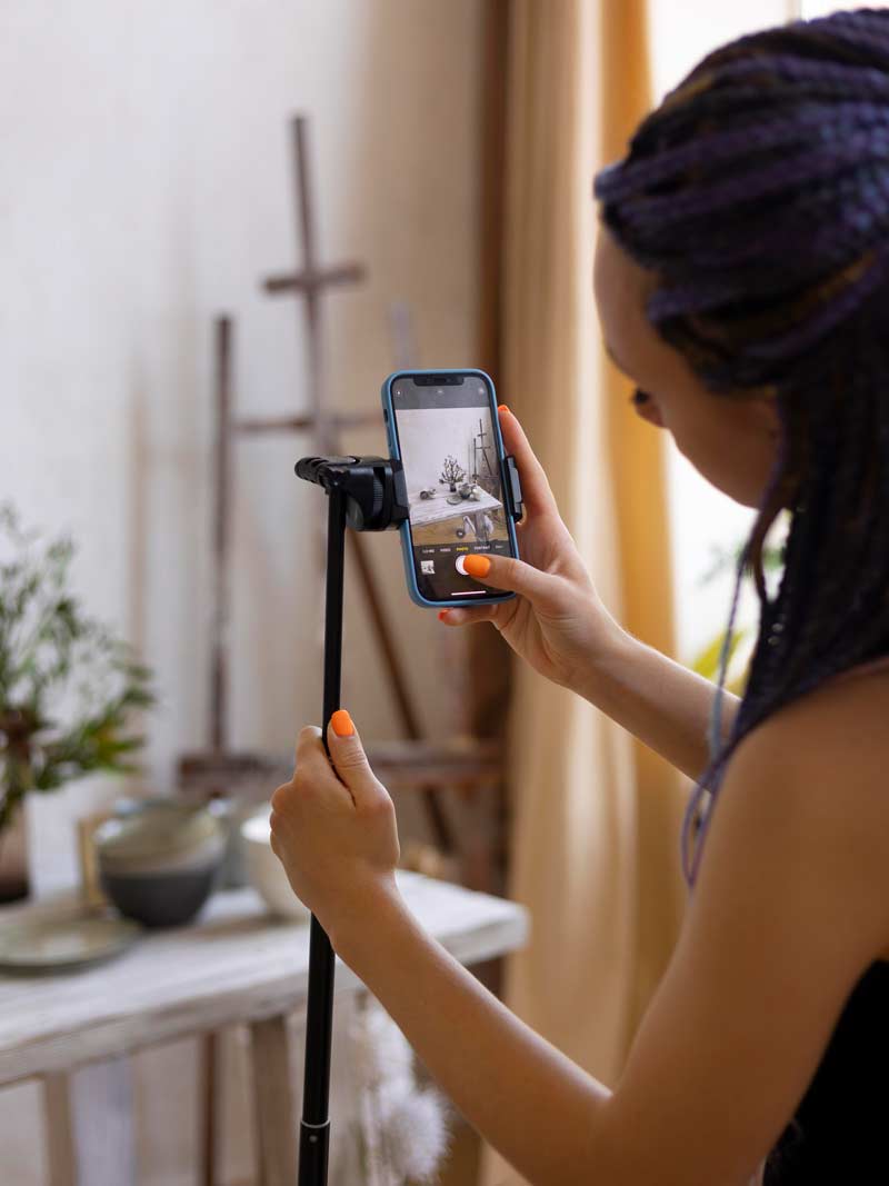 زن در حال عکاسی با موبایل روی تک پایه